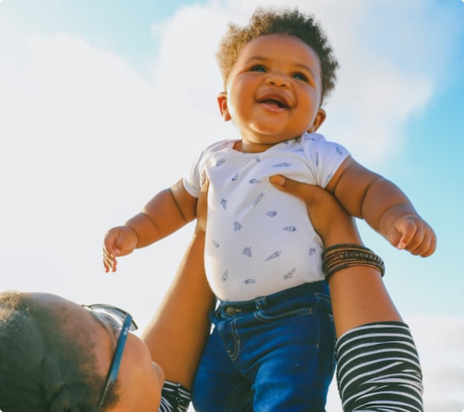 Woman raising a happy baby in the air on a beach.