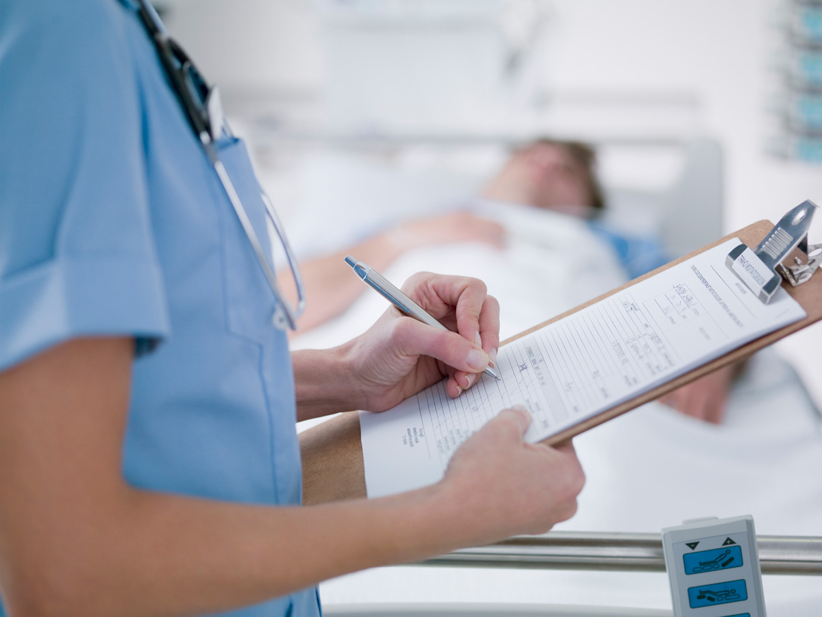 Nurse or doctor making note on patients chart within hospital room