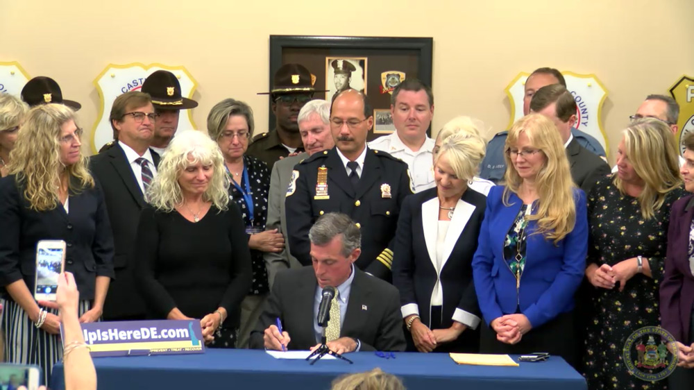 Delaware governor signing bill, surrounded by public officials